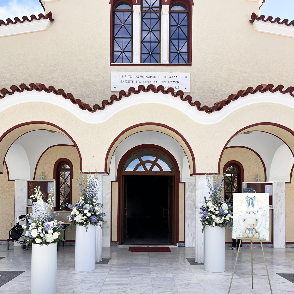 Διακόσμηση βάπτισης αγοριού στον Ιερό Ναό Αγίου Νικολάου Γλυφάδας με μπλε και λευκά λουλούδια, teddy bear θέμα και κομψό στολισμό εισόδου.